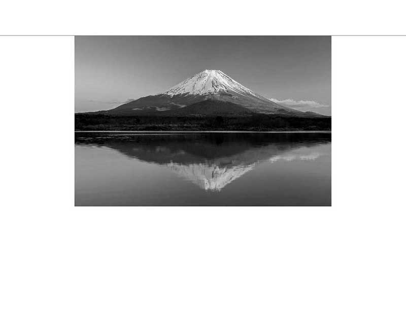 Schwarz-Weiß-Fotografie des Fujisan mit Spiegelung Schwarz-Weiß-Bild des Fujisan, dessen schneebedeckter Gipfel sich im ruhigen Wasser spiegelt