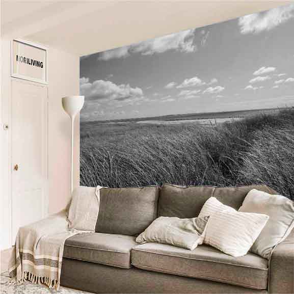 Modernes Wohnzimmer mit beige-grauem Sofa, mehreren Kissen, Stehlampe und großflächigem Naturbild mit Wiesenlandschaft an der Wand.