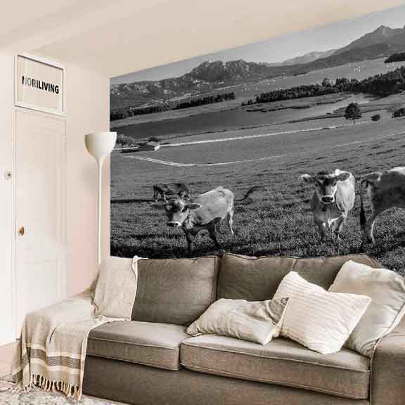 Wohnzimmer mit grauem Sofa und großem Wandbild von Kühen in einer Berglandschaft