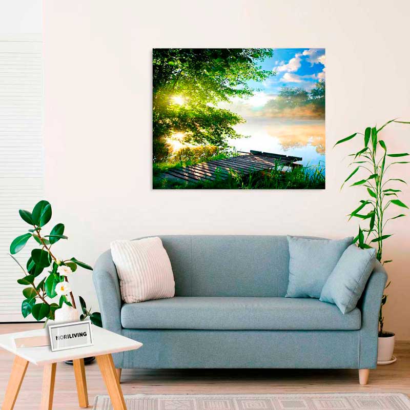 Wohnzimmer mit blauer Couch, Zimmerpflanzen und Wandbild mit Naturmotiv am See