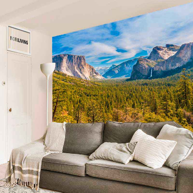 Ein Wohnzimmer mit grauem Sofa und Fototapete einer Berglandschaft im Hintergrund